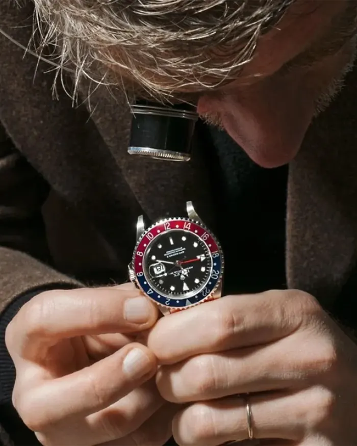 Expert examining a luxury Rolex GMT-Master watch with a loupe